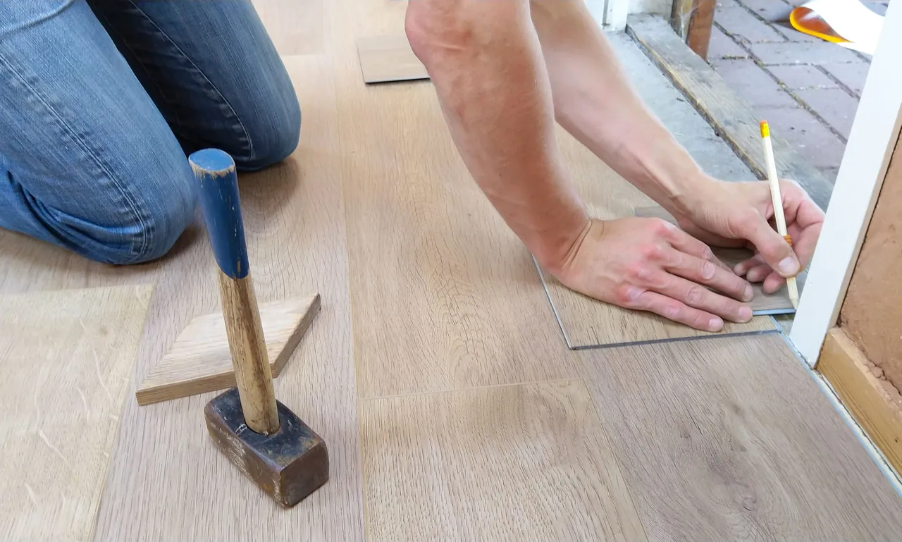 Asentaja merkitsee kynällä lattialaminaatin palaa keskeneräisellä lattialla.